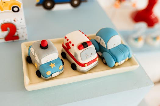 Three fondant toy cars, a police car, ambulance, and sedan on a plate.