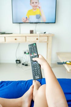 A person holding a remote control while watching TV indoors.