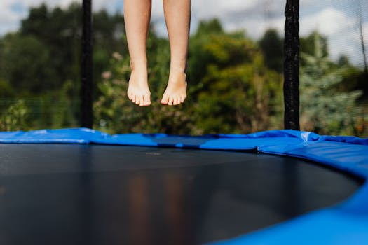 A child's bare feet captured mid-jump on a trampoline outdoors in a sunlit summer setting.