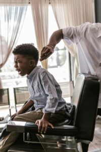 Young boy receiving a haircut in a barber shop, captured indoors with natural light.