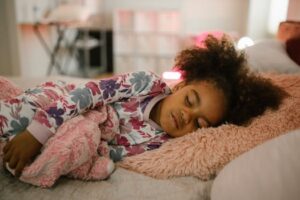 A young girl in floral pajamas peacefully sleeping with toys in a comfortable bedroom setting.